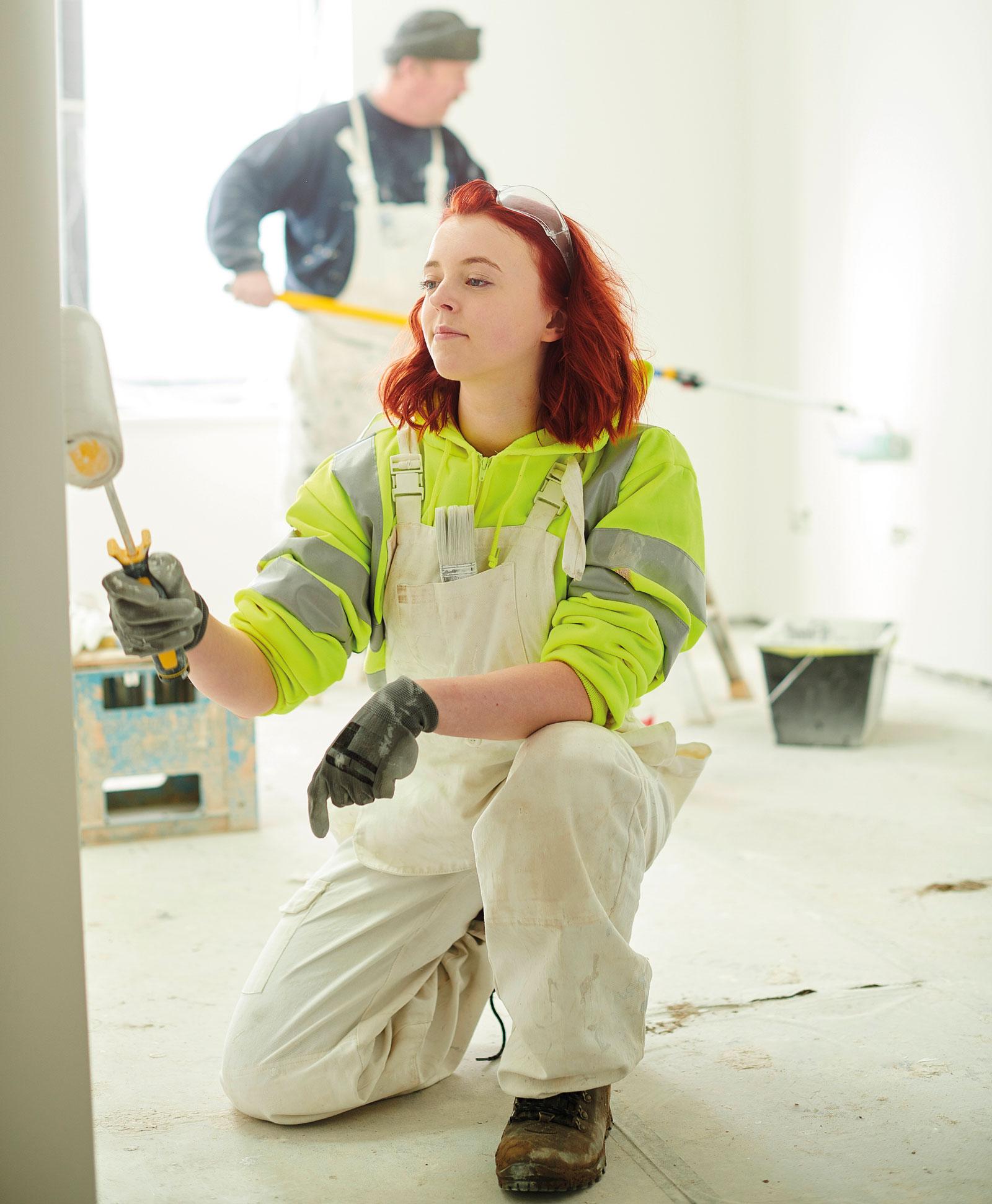Photograph of a young woman decorator painting a wall with a roller.