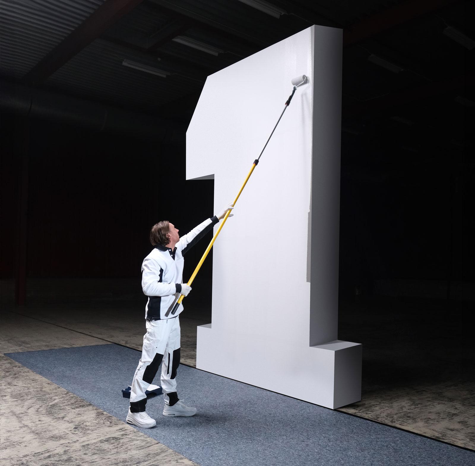 Photograph of a decorator painting a giant number one with a roller.