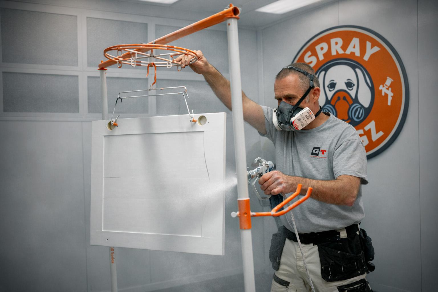 Photograph of a painter spraying a kitchen cabinet door
